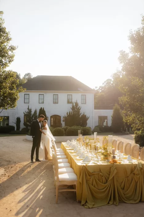 Couple embraces beside a long golden reception table during golden hour at The Bradford NC.