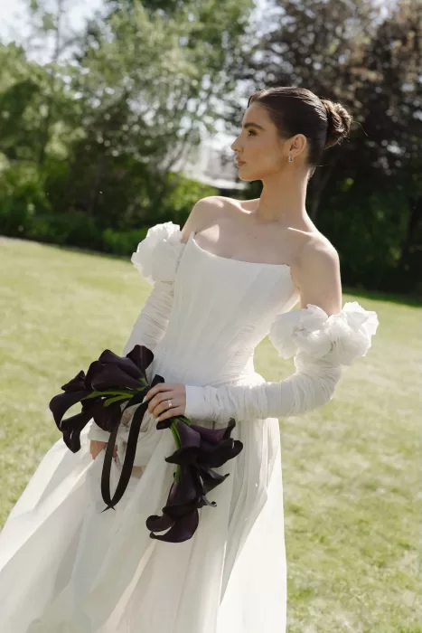 Bride in structured gown holding deep plum calla lilies at Treelove Parkas, captured in soft morning light.