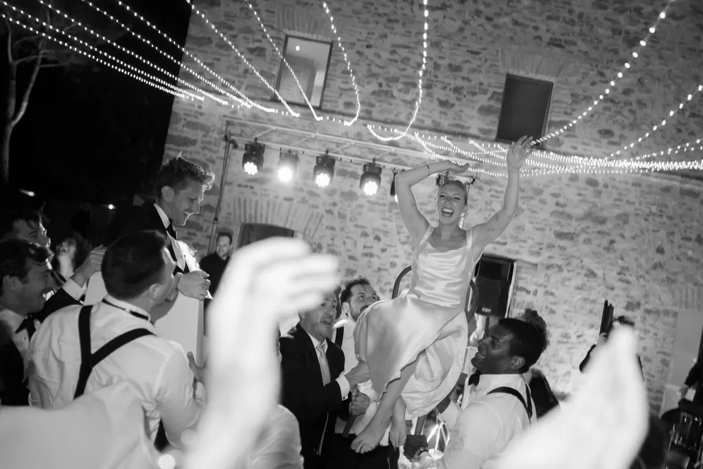 Bride and groom lifted on chairs during a joyful wedding celebration at Casa Olivi under string lights.