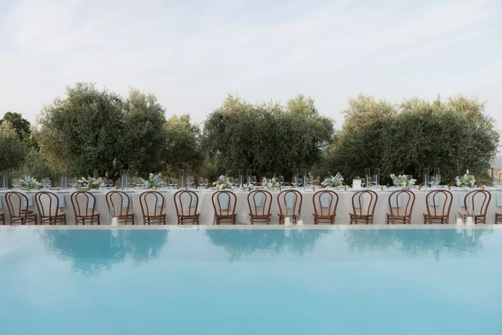 Long wedding table beside the pool at Casa Olivi, surrounded by olive trees and floral centrepieces.