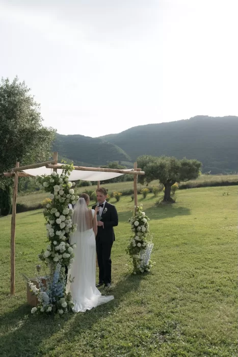 The bride and groom exchange vows beneath a floral ceremony arch in the hills at Casa Olivi.