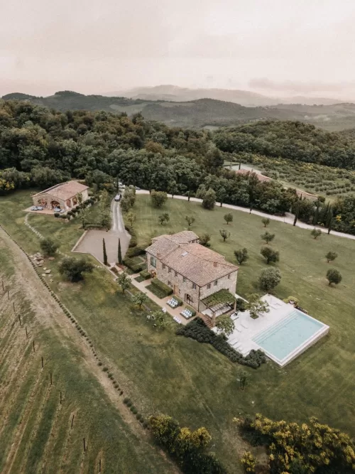 Aerial view of Castello di Casole surrounded by Tuscan hills and vineyards on a misty day.