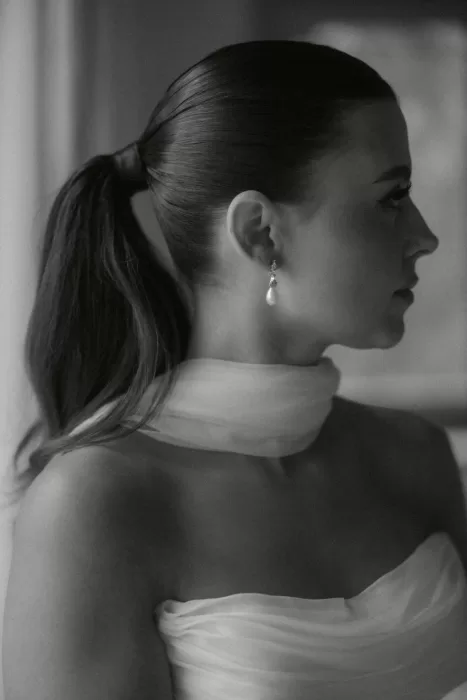 Elegant black-and-white portrait of the bride in soft natural light, wearing pearl earrings and a sheer scarf at Castello di Casole.