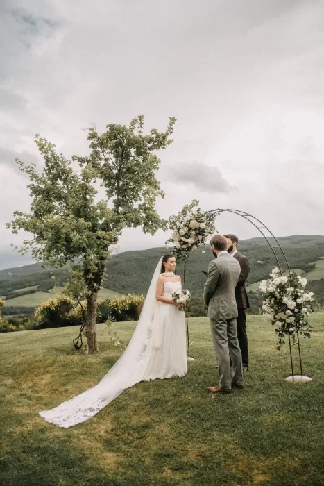 Bride and groom exchanging vows under floral arch with Tuscan hills at Castello di Casole.