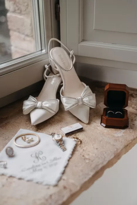Elegant flatlay of bridal shoes, rings, and heirloom jewellery with Castello di Casole keepsake.