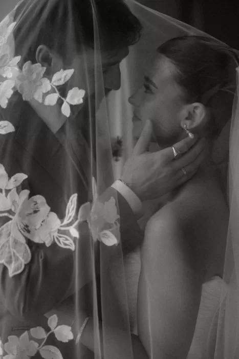 Romantic black-and-white portrait of the couple sharing a quiet moment under a floral-embroidered veil.
