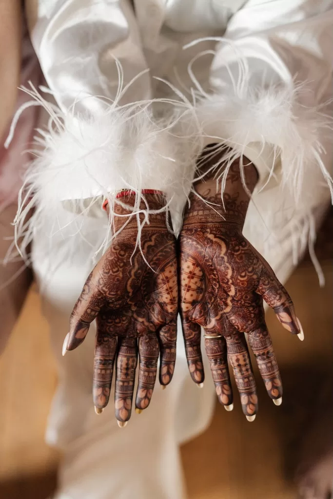 Intricate henna designs on the bride’s hands with feather-trimmed satin sleeves
