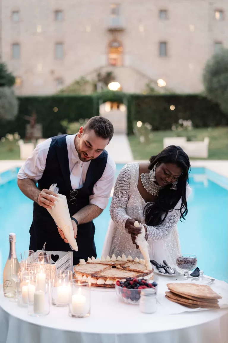 Bride and groom decorating their wedding cake by the pool at Castello di Montignano