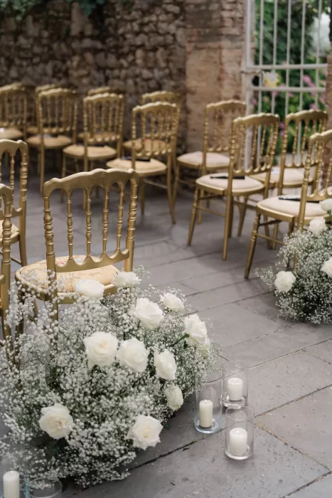 Romantic ceremony setup at Castello di Montignano with gold chairs, white roses, and soft candlelight.