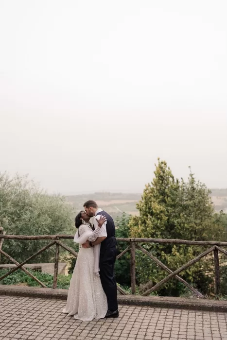 Bride and groom share a kiss on a cobbled path with Castello di Montignano's rolling hills in the background.