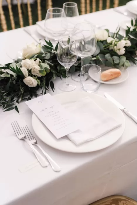 Elegant reception table setting at Castello di Montignano with greenery, white roses, and a printed menu.