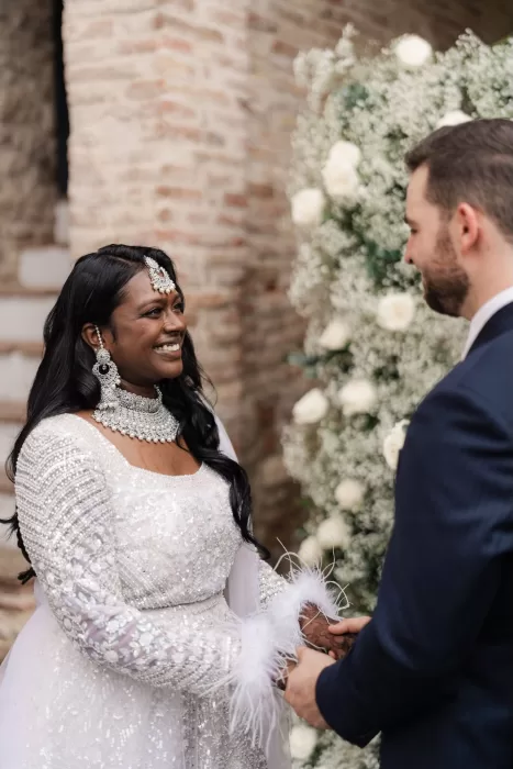 Bride and groom smiling at each other during their vows, surrounded by white roses at Castello di Montignano