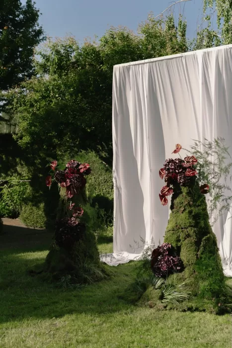 Bold floral installations of moss and burgundy blooms framing the ceremony space at Treelove Parkas.