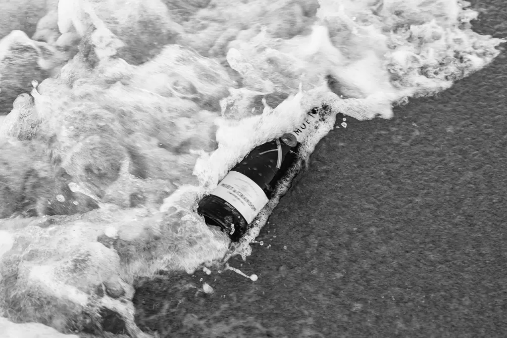 A Moët champagne bottle is swept up by a crashing wave, captured in crisp black and white.