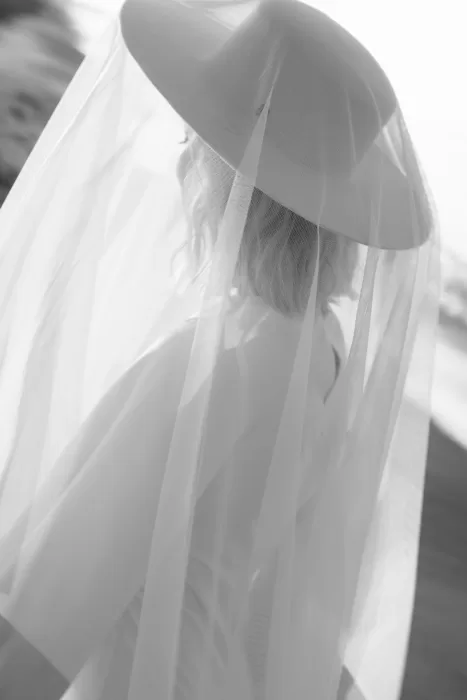 A soft close-up of the bride’s hat and veil, with delicate textures and gentle shoreline light.