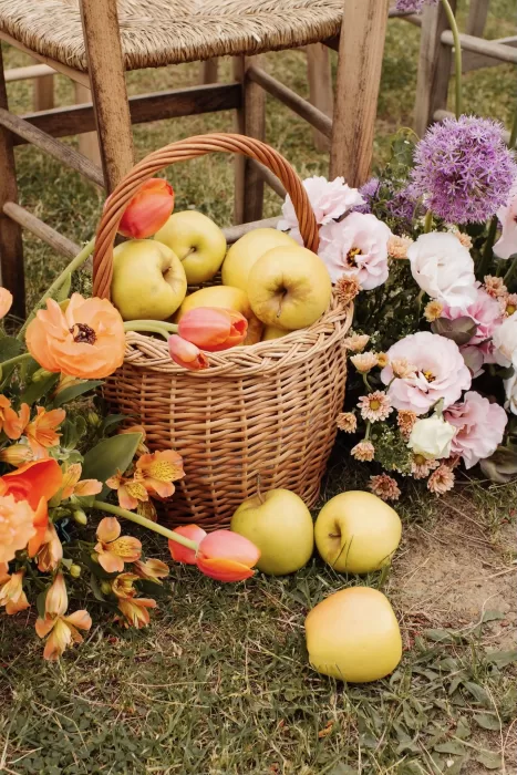 Basket of yellow apples and vibrant flowers by rustic ceremony chairs at Conti di San Bonifacio.