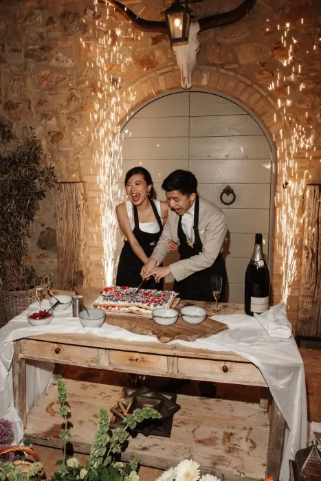 Bride and groom laughing while cutting cake with indoor sparklers at Conti di San Bonifacio.