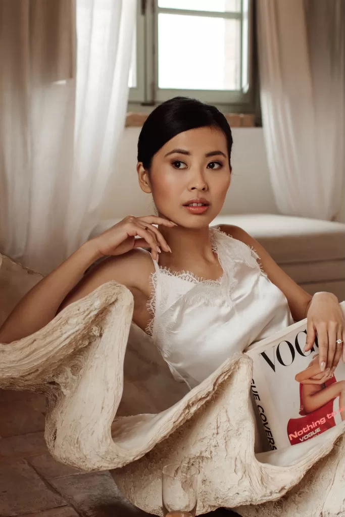 Bride relaxing indoors in a sculptural shell chair holding Vogue, with soft natural light at Conti di San Bonifacio.