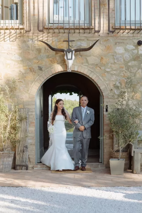 Bride walking arm in arm with her father through the stone arch at Conti di San Bonifacio.