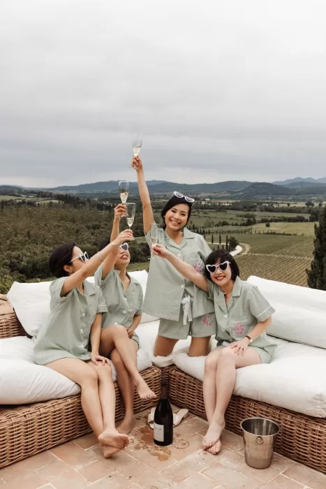 Bridesmaids in matching pyjamas raising glasses on a terrace overlooking the Tuscan hills at Conti di San Bonifacio.