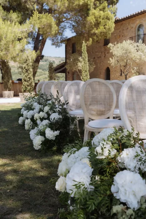 Ceremony chairs lined with white flowers on the lawn at Conti di San Bonifacio, with stone villa in the background.
