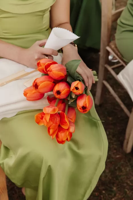 Wedding guest in green dress holding a vibrant orange tulip bouquet during the ceremony at Conti di San Bonifacio.