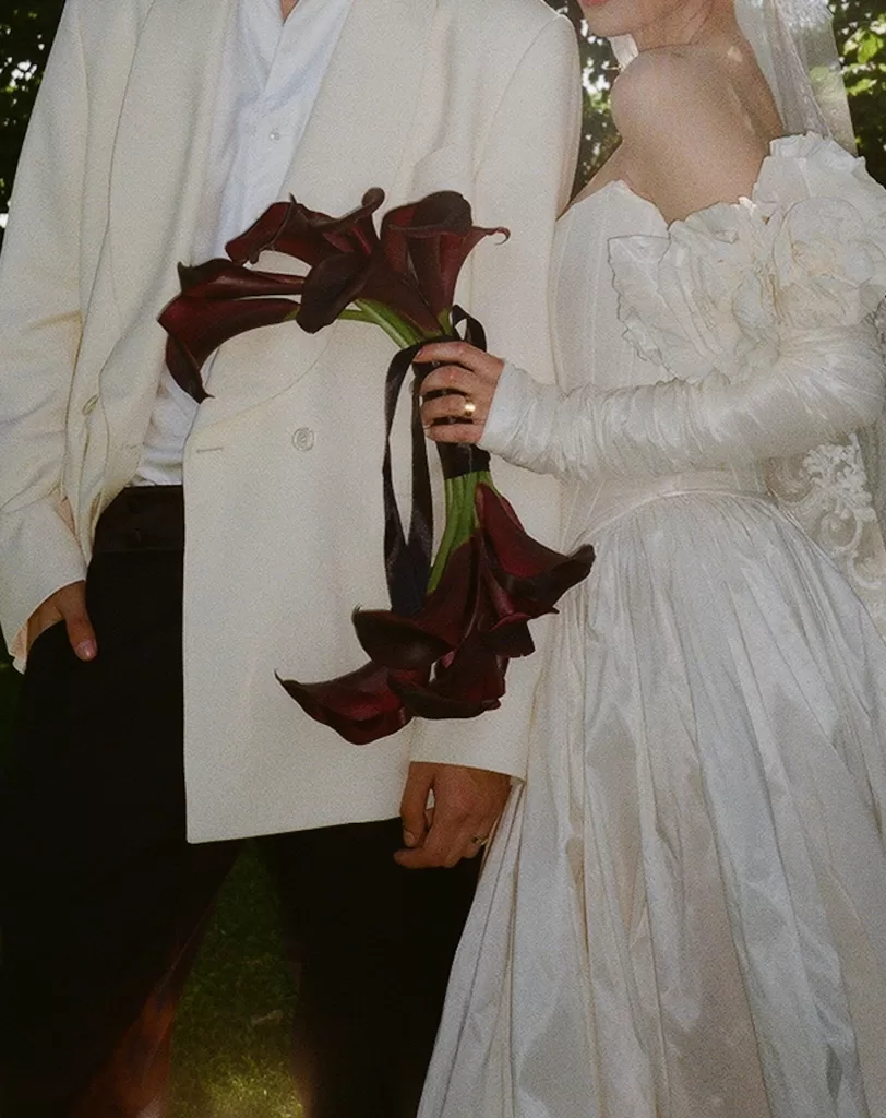 Bride and groom standing close, calla lily bouquet in hand, surrounded by dappled light at Treelove Parkas.