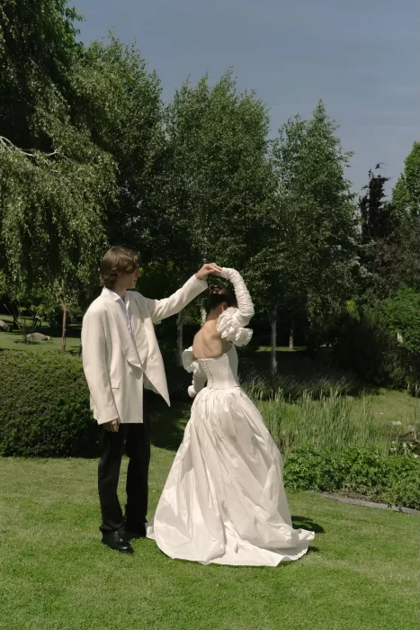 Groom twirls the bride on a sunlit lawn at Treelove Parkas, surrounded by lush greenery.