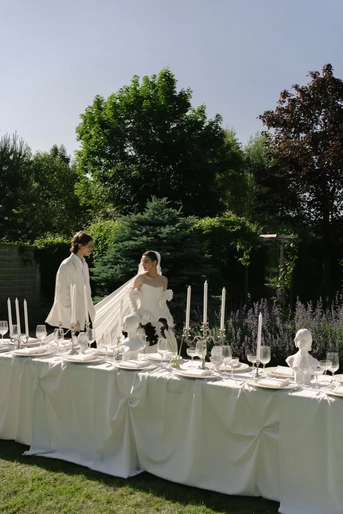 Bride and groom walking beside an elegant candlelit dinner table in the gardens of Treelove Parkas.