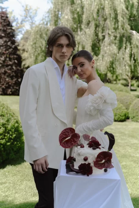 Elegant couple posing beside their modern wedding cake in the gardens of Treelove Parkas.