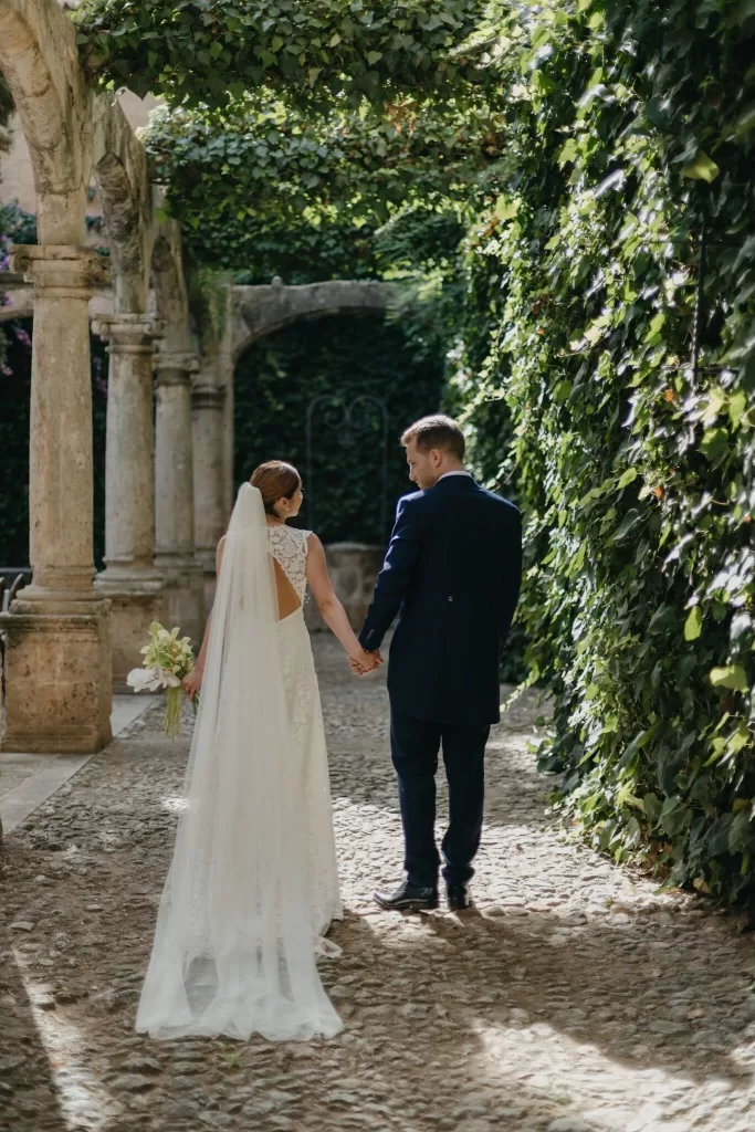 Bride and groom walking hand in hand through ivy-lined corridor at Finca Es Convent.