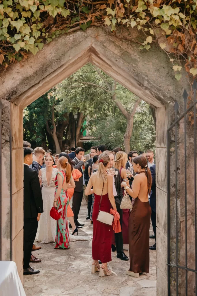 Wedding guests mingling during cocktail hour under ivy-covered stone arch at Finca Es Convent