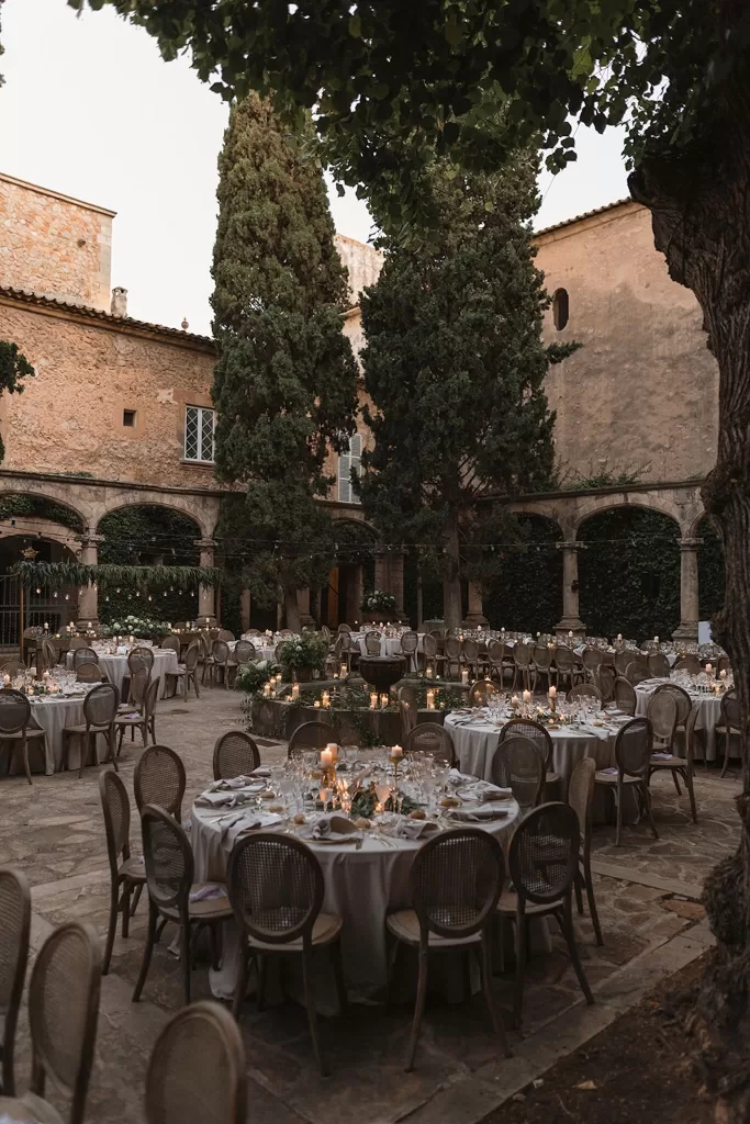 Outdoor reception at Finca Es Convent with candlelit round tables and historic stone arches