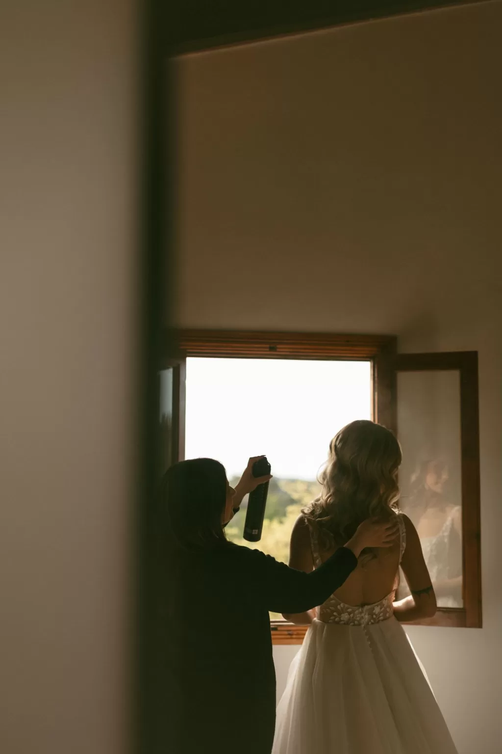 Bride having her hair styled by the window with soft golden light filling the room at Finca Son Collell