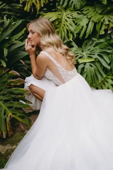 A serene moment as the bride sits among lush monstera leaves in her embroidered gown at Finca Son Collell.