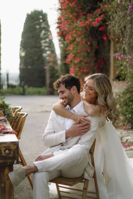 A tender moment as the bride embraces the groom beside a rustic wooden table at Finca Son Collell, surrounded by flowers.
