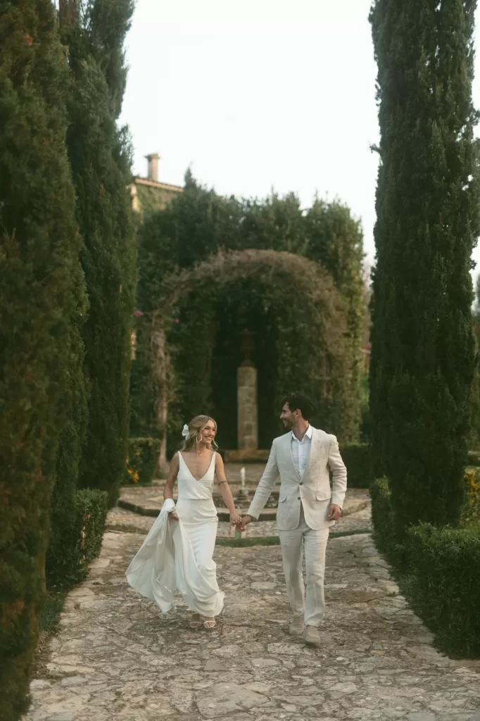 Bride and groom walking hand in hand through a cypress-lined path at Finca Son Collell