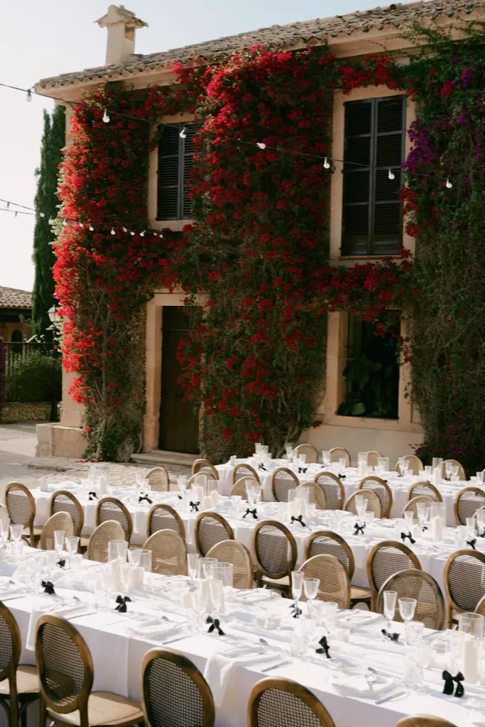 Wedding tables set beneath the flower-covered facade of Finca Son Collell, with string lights overhead.