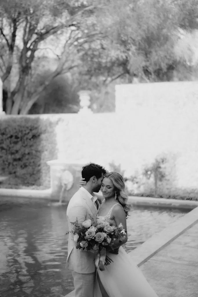 An intimate embrace beside a tranquil fountain, the bride holding a vibrant bouquet at Finca Son Collell.