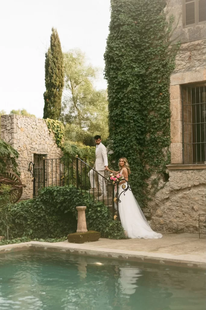Bride and groom posing on ivy-covered garden staircase beside the pool at Finca Son Collell
