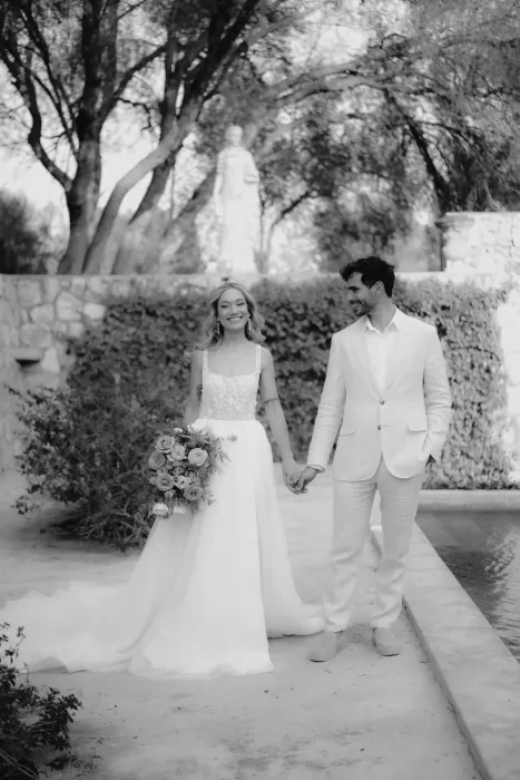 The couple walk hand in hand through a peaceful garden courtyard at Finca Son Collell, beaming with joy.