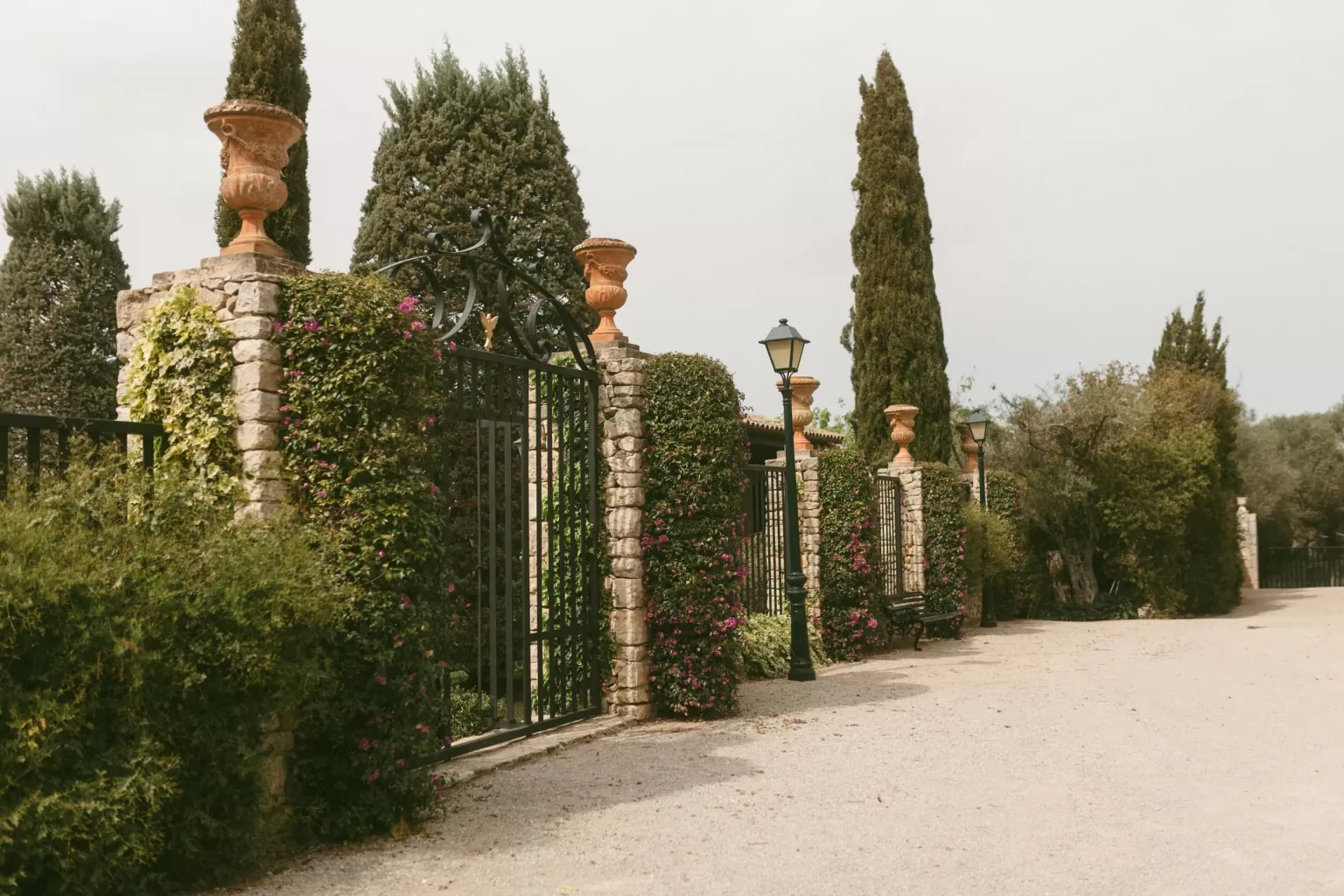 Stone gate covered in climbing greenery and flowers at Finca Son Collell, lined with cypress trees and lanterns