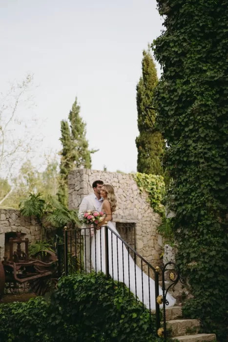 The couple pose on a stone staircase wrapped in ivy, surrounded by timeless Mediterranean charm at Finca Son Collell.