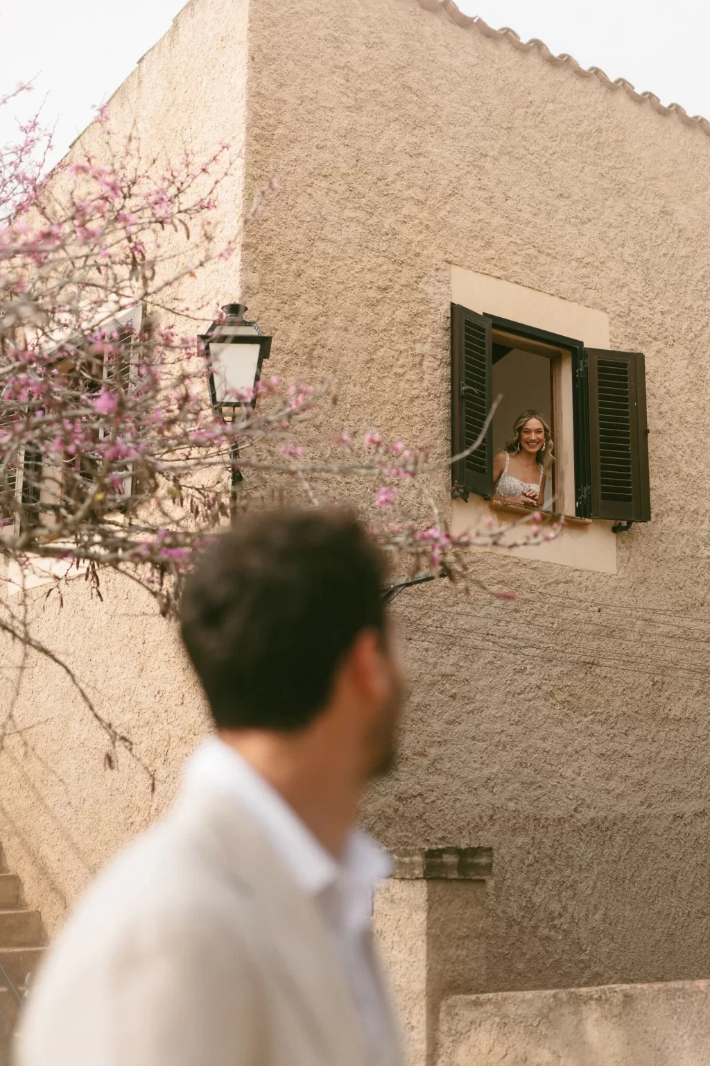 Bride smiling down from a window framed by shutters and spring blossoms at Finca Son Collell