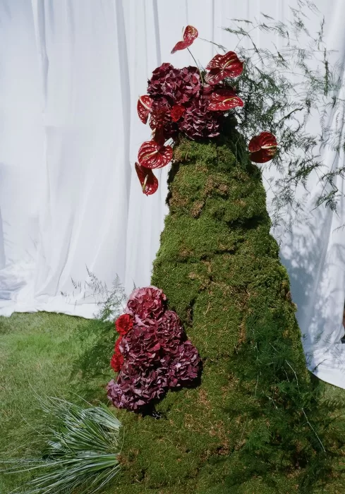 Moss-covered ceremony sculpture adorned with burgundy hydrangeas and red anthuriums at Treelove Parkas.