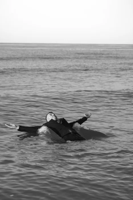 The groom floats effortlessly on calm ocean waters, arms spread wide in a moment of quiet release.