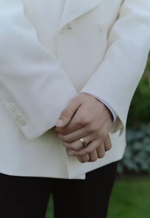 Close-up of groom’s hands with gold wedding band and cream suit at Treelove Parkas.