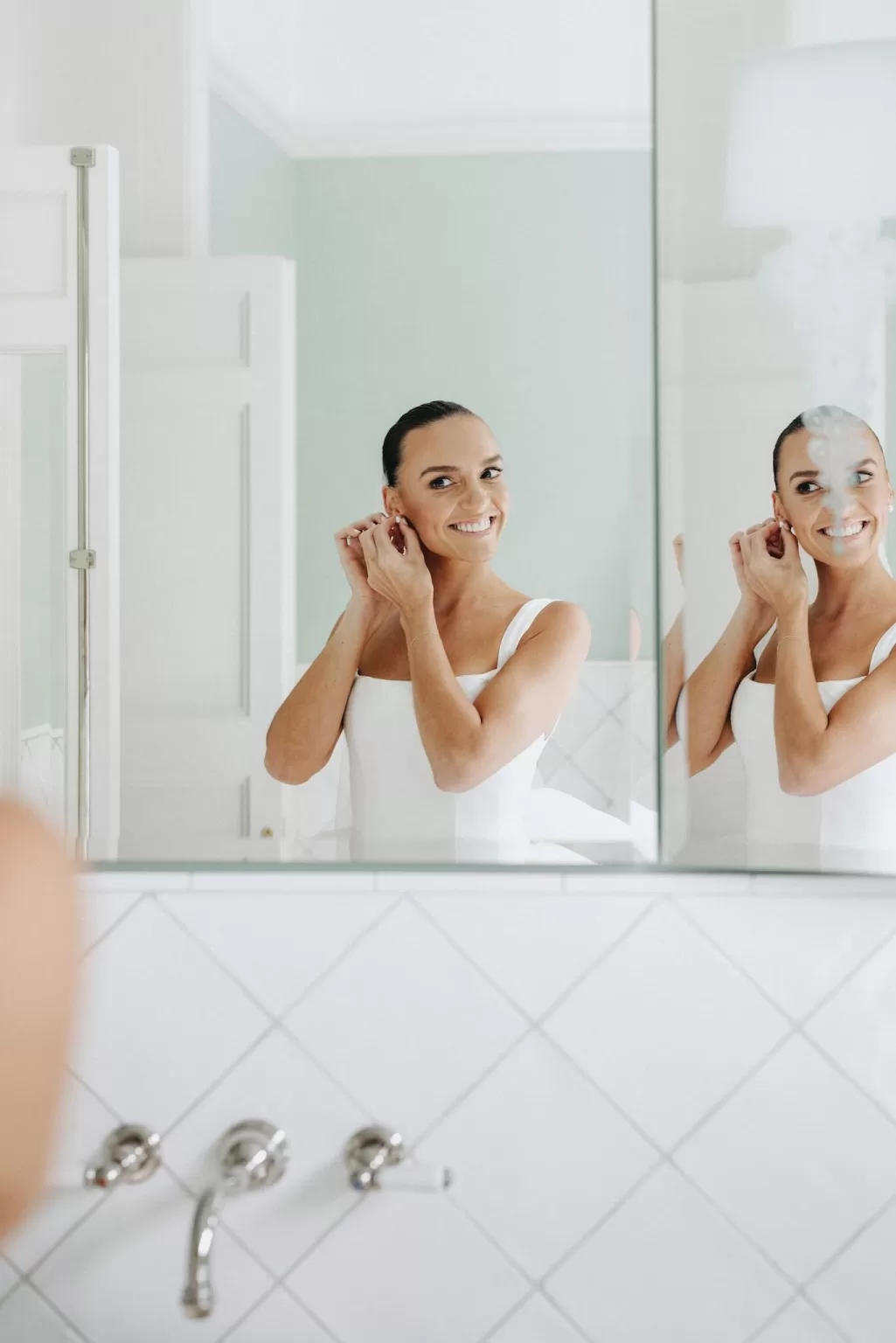 Bride smiling as she puts on earrings in front of the mirror before her wedding at Le Mas Barossa.