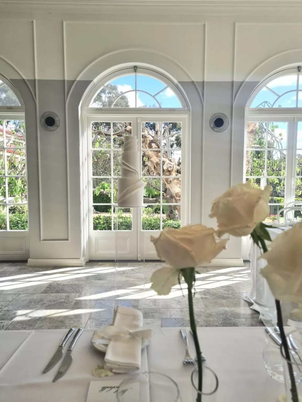 Elegant indoor dining space at Le Mas Barossa with arched glass doors opening to a lush garden, styled with minimalist floral decor.