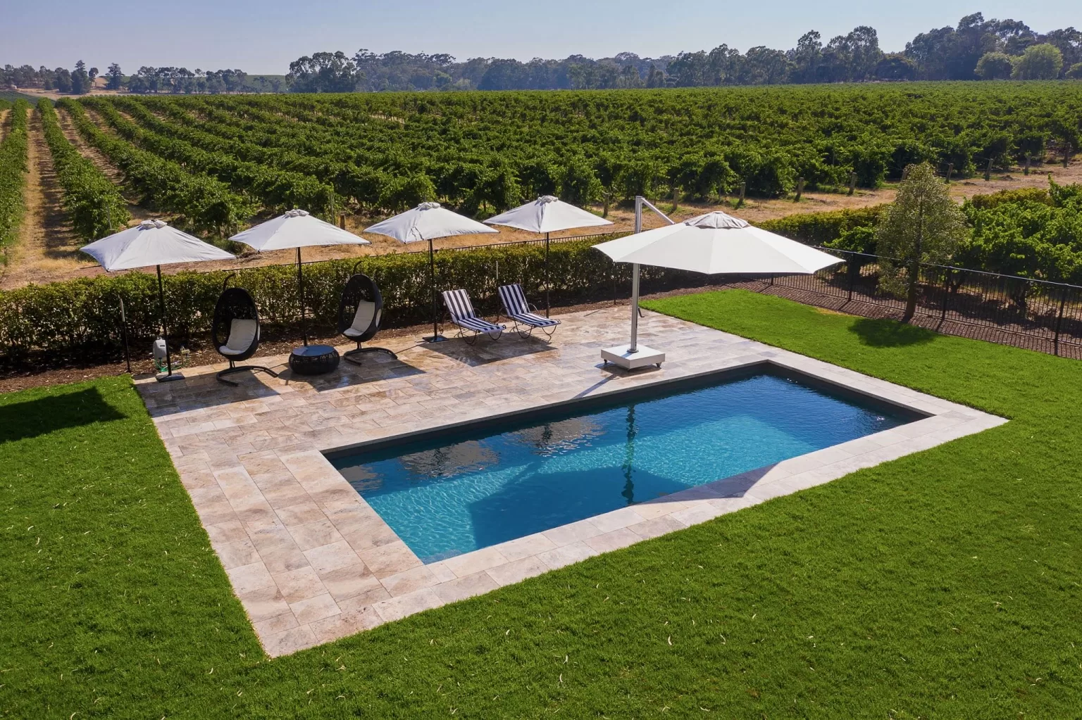 Chic poolside area with vineyard backdrop under sun umbrellas at Le Mas Barossa